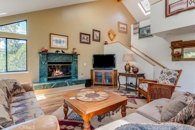 living area with high vaulted ceiling, a fireplace, beamed ceiling, a skylight, and wood finished floors