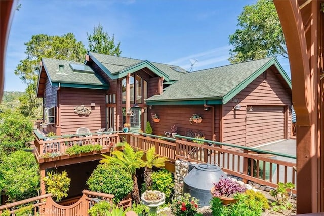 back of property with roof with shingles, a deck, and a detached garage