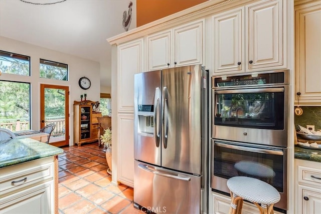 kitchen featuring light tile patterned floors, cream cabinets, backsplash, and appliances with stainless steel finishes