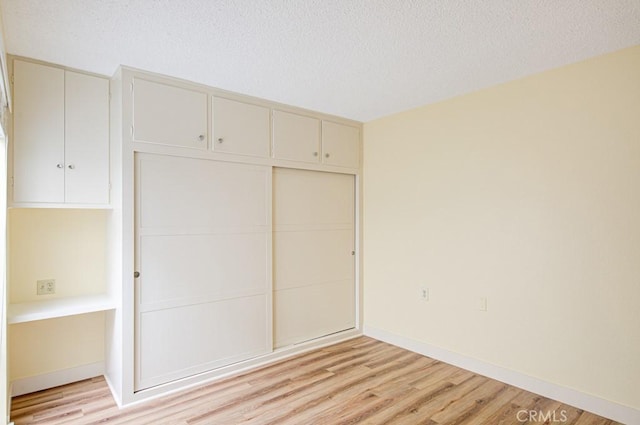 523 Calle Aragon Unit C, Laguna Woods, CA 92637 - unfurnished bedroom with a closet, light wood-style flooring, baseboards, and a textured ceiling