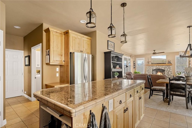 kitchen with light tile patterned floors, a ceiling fan, freestanding refrigerator, and light brown cabinetry