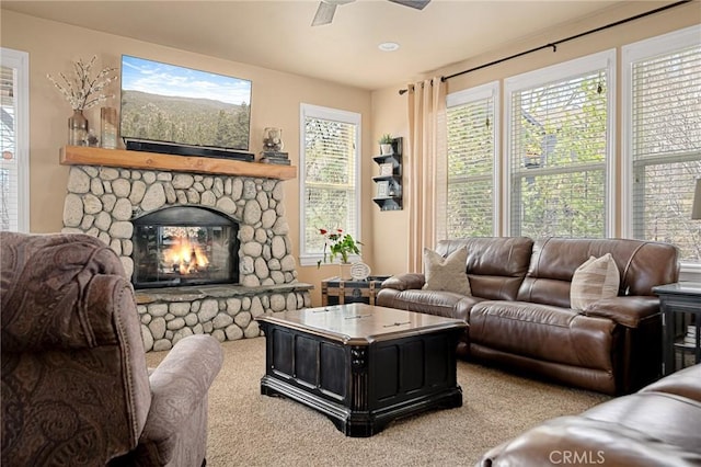 living room featuring carpet floors, a stone fireplace, and a ceiling fan