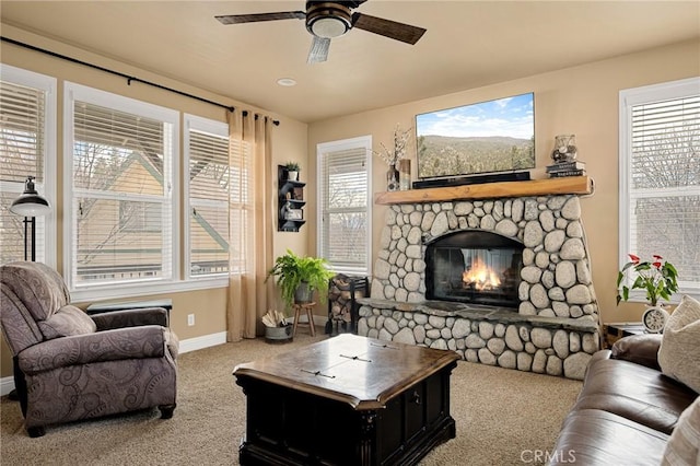 carpeted living area with ceiling fan, baseboards, a stone fireplace, and a wealth of natural light