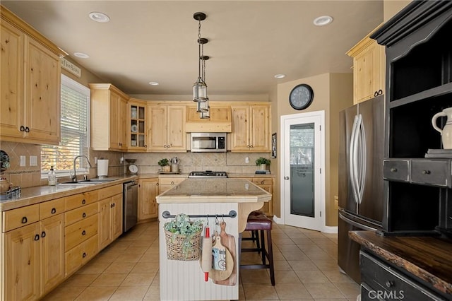 kitchen featuring light tile patterned floors, a kitchen island, a sink, stainless steel appliances, and light brown cabinets