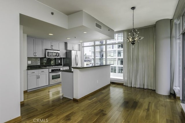 kitchen with dark wood finished floors, dark countertops, stainless steel appliances, a notable chandelier, and backsplash