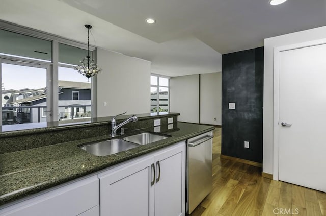 kitchen featuring light wood-type flooring, white cabinets, dark stone countertops, dishwasher, and a sink