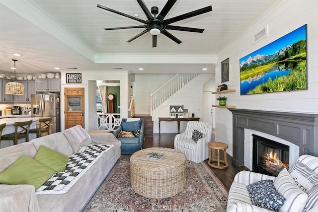 living room featuring a glass covered fireplace, stairway, crown molding, ceiling fan, and wood finished floors
