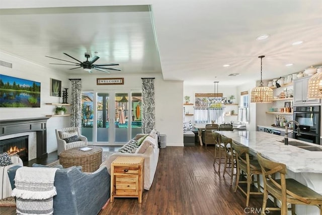 living room featuring a ceiling fan, a glass covered fireplace, recessed lighting, baseboards, and dark wood-style floors