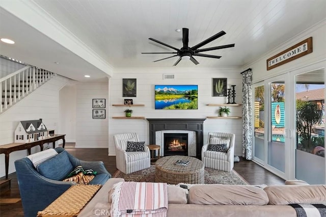 living room with ceiling fan, a lit fireplace, ornamental molding, visible vents, and wood finished floors