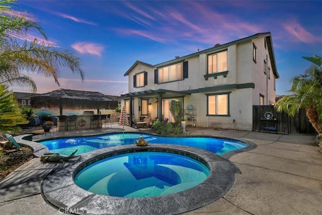 pool at dusk with a patio area, a pool with connected hot tub, and outdoor dry bar