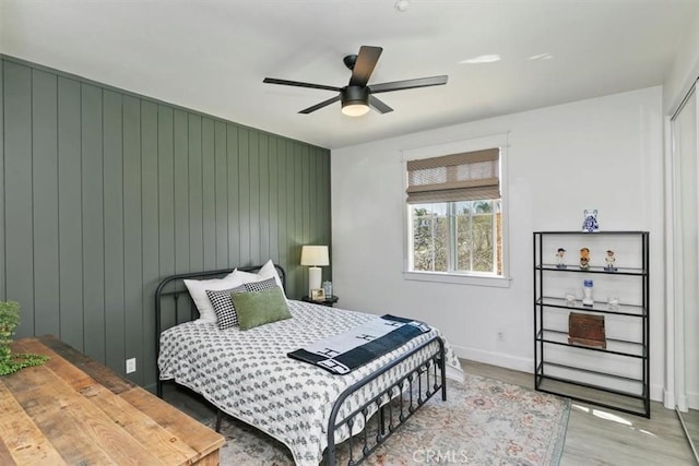 bedroom featuring wood walls, baseboards, a ceiling fan, and wood finished floors