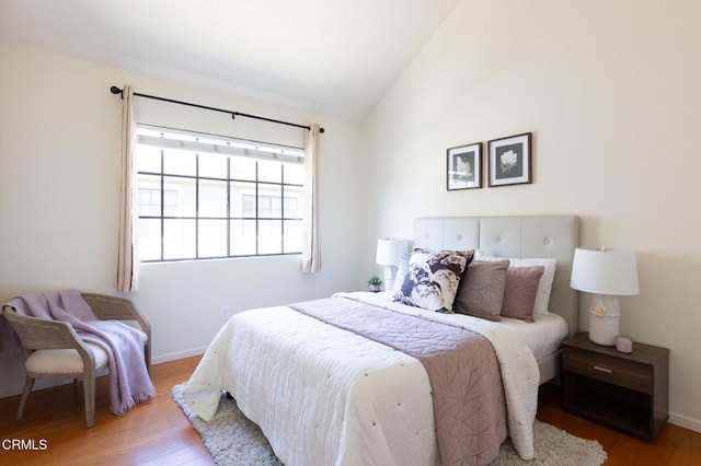 bedroom with light wood finished floors, baseboards, and vaulted ceiling