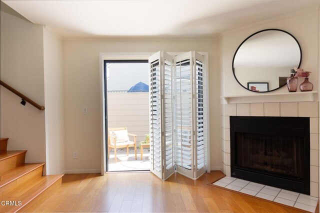 doorway to outside featuring stairs, a tiled fireplace, light wood-type flooring, and crown molding
