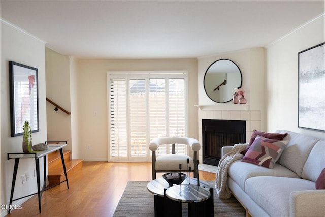 living room featuring a tiled fireplace, ornamental molding, plenty of natural light, and wood finished floors