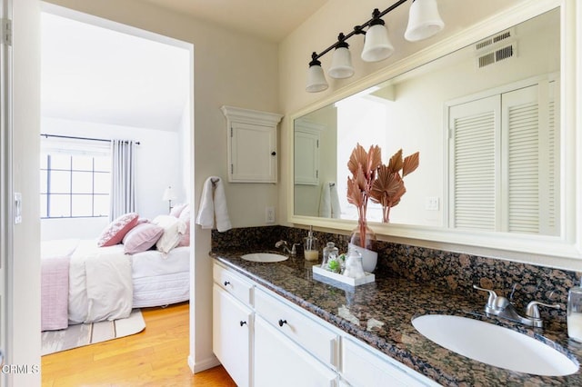 bathroom with double vanity, ensuite bath, a sink, and wood finished floors