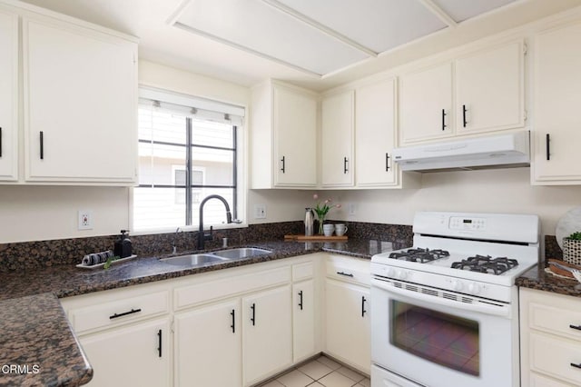 kitchen featuring dark stone counters, white cabinetry, white range with gas stovetop, under cabinet range hood, and a sink