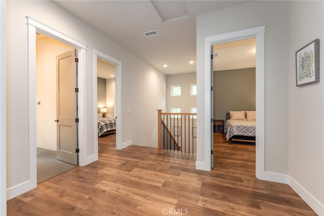 hallway featuring visible vents, baseboards, wood finished floors, and an upstairs landing
