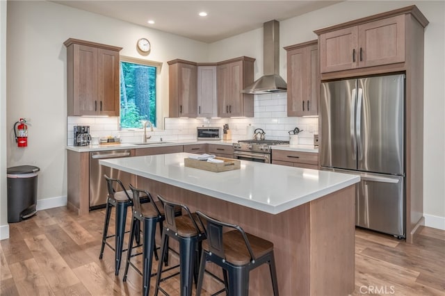 kitchen featuring wall chimney range hood, a sink, light wood finished floors, a kitchen breakfast bar, and stainless steel appliances