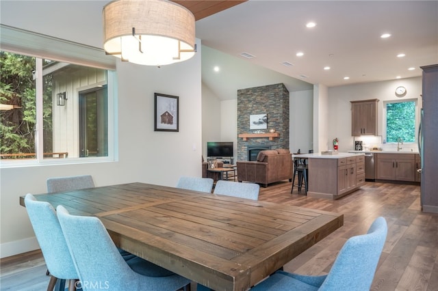 dining space featuring a stone fireplace, visible vents, vaulted ceiling, wood finished floors, and recessed lighting