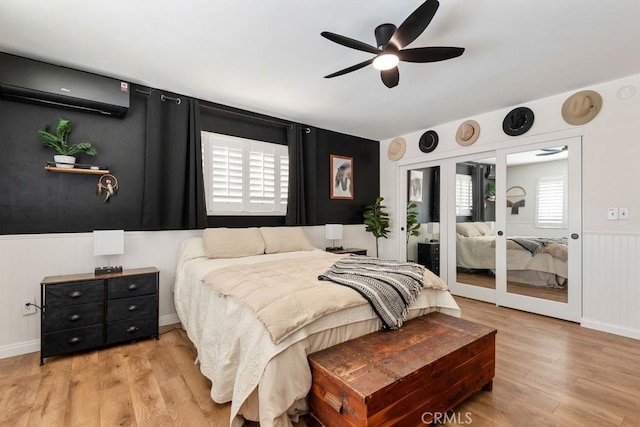 bedroom featuring a ceiling fan, a wall unit AC, light wood-style flooring, and a wainscoted wall