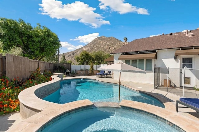 view of pool with a fenced backyard, a pool with connected hot tub, a mountain view, and a patio area