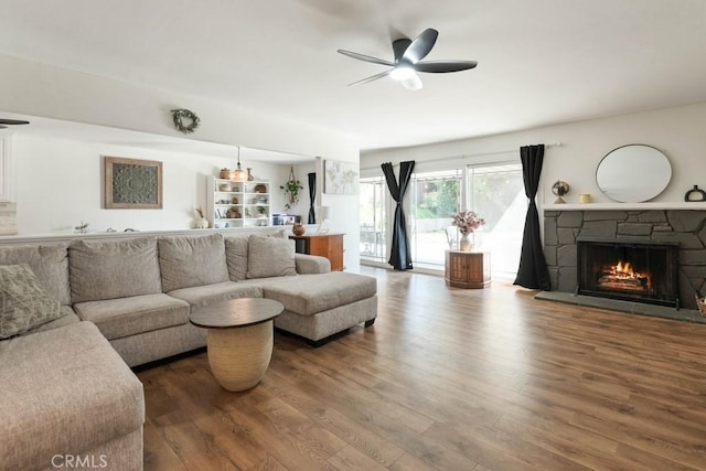 living area with a stone fireplace, a ceiling fan, and wood finished floors