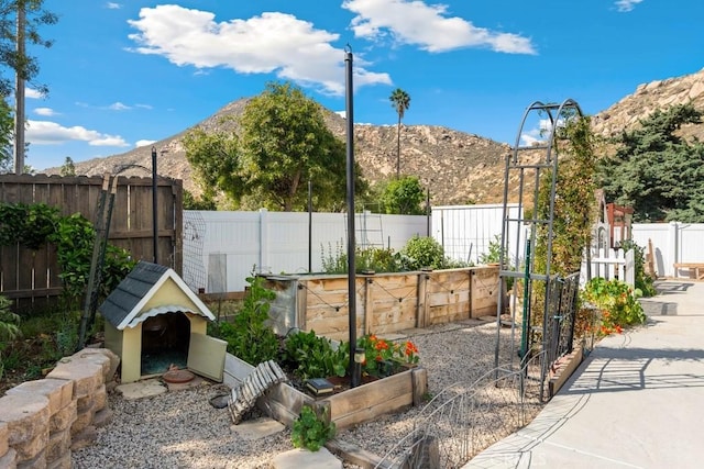 view of patio / terrace featuring fence, a mountain view, and a vegetable garden