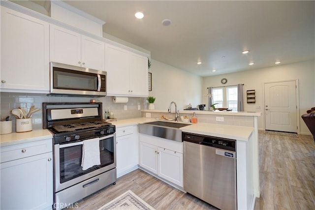 kitchen featuring stainless steel appliances, a peninsula, a sink, white cabinetry, and backsplash