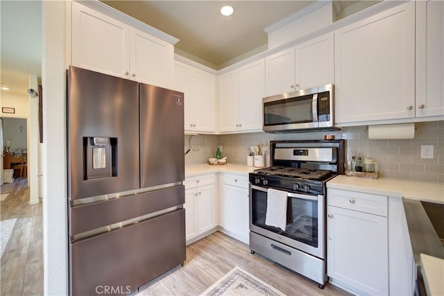 kitchen with stainless steel appliances, light wood-type flooring, white cabinetry, light countertops, and backsplash