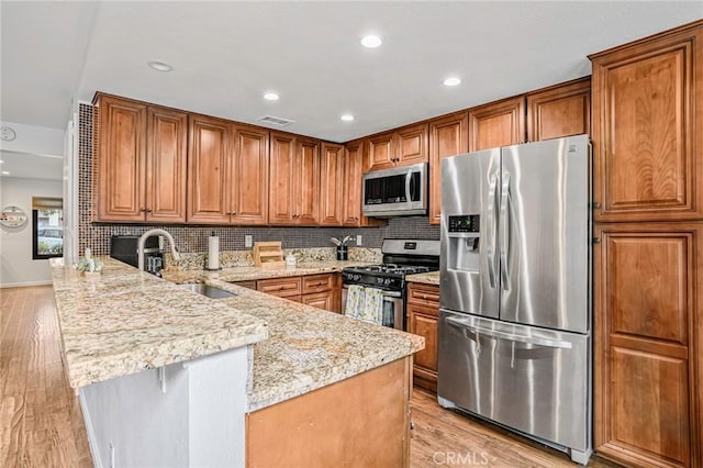 kitchen with a peninsula, brown cabinets, light stone counters, a sink, and stainless steel appliances