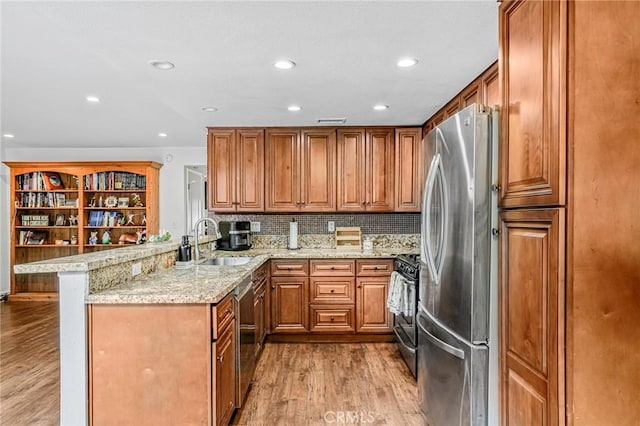 kitchen with appliances with stainless steel finishes, brown cabinets, a sink, a peninsula, and light wood-style flooring