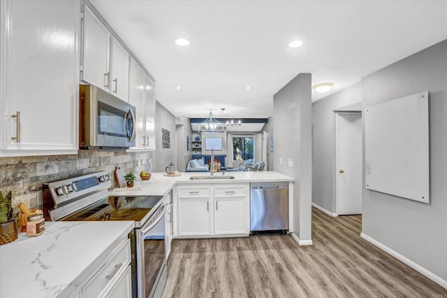 kitchen with white cabinets, appliances with stainless steel finishes, light wood finished floors, baseboards, and tasteful backsplash