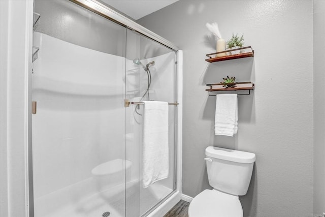 bathroom featuring toilet, wood finished floors, and a stall shower