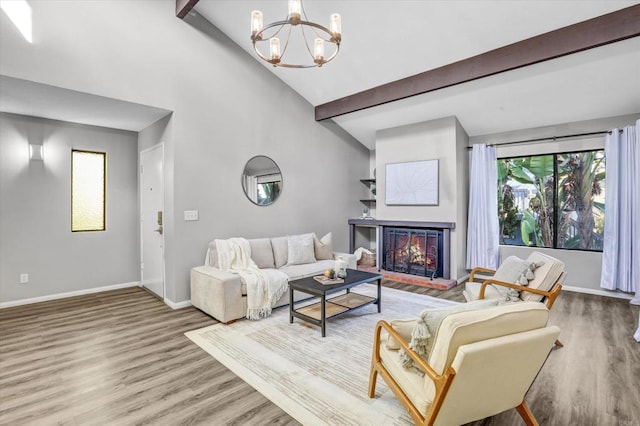 living room with wood finished floors, beam ceiling, baseboards, a warm lit fireplace, and a chandelier