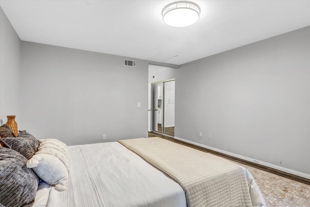 bedroom with baseboards, visible vents, wood finished floors, and a closet