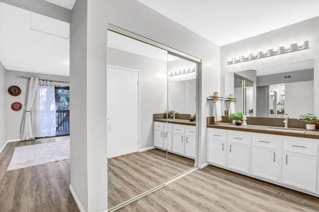 bathroom featuring a sink, baseboards, two vanities, wood finished floors, and visible vents