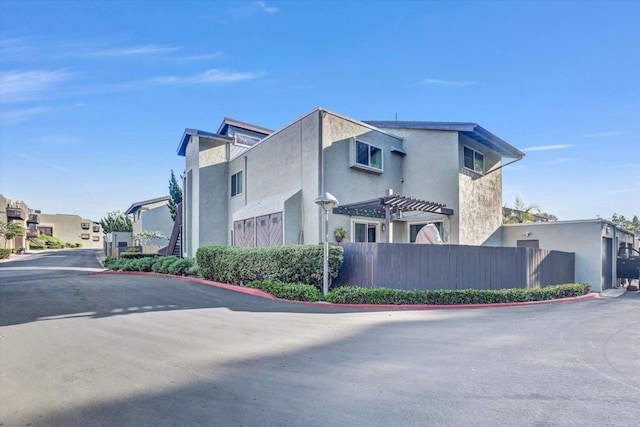 view of property exterior featuring stucco siding, a pergola, a residential view, and fence