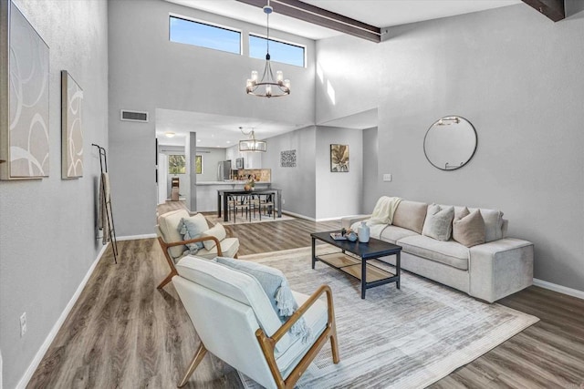 living area with an inviting chandelier, visible vents, a towering ceiling, beamed ceiling, and baseboards