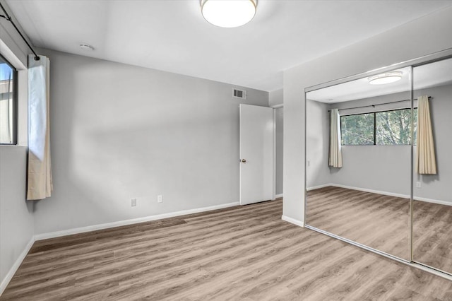 unfurnished bedroom with visible vents, baseboards, wood finished floors, and a closet