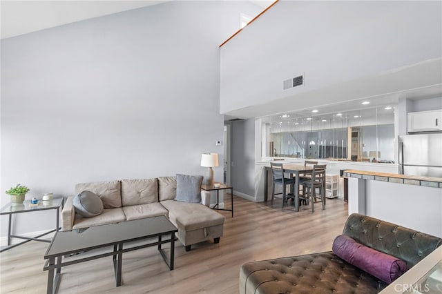 living area with light wood-type flooring, visible vents, recessed lighting, a high ceiling, and baseboards