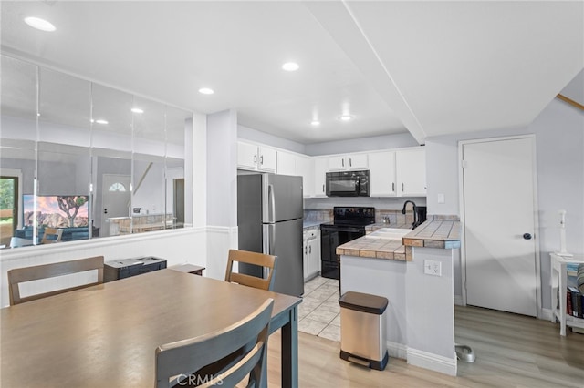 kitchen featuring light wood-type flooring, recessed lighting, a peninsula, white cabinetry, and black appliances