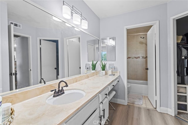 bathroom featuring baseboards, double vanity, visible vents, a sink, and wood finished floors