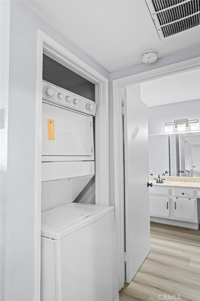 laundry room with laundry area, stacked washer and dryer, visible vents, a sink, and light wood finished floors