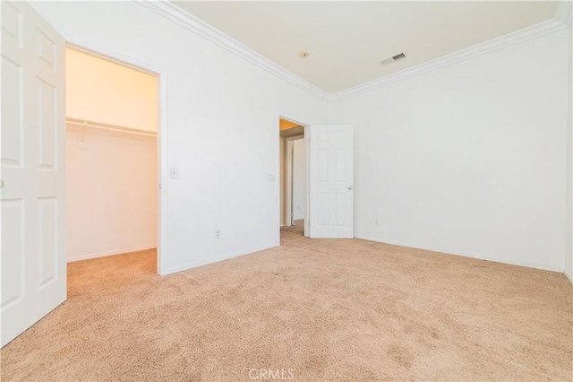 unfurnished bedroom featuring a walk in closet, visible vents, carpet, and ornamental molding