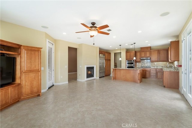 kitchen featuring ceiling fan, brown cabinetry, a kitchen island, appliances with stainless steel finishes, and under cabinet range hood