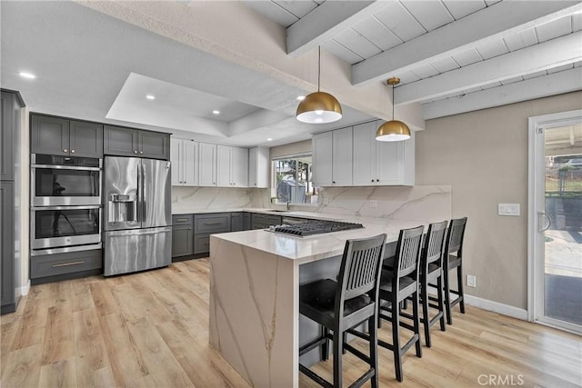 kitchen with light wood-type flooring, appliances with stainless steel finishes, a peninsula, light stone countertops, and decorative backsplash