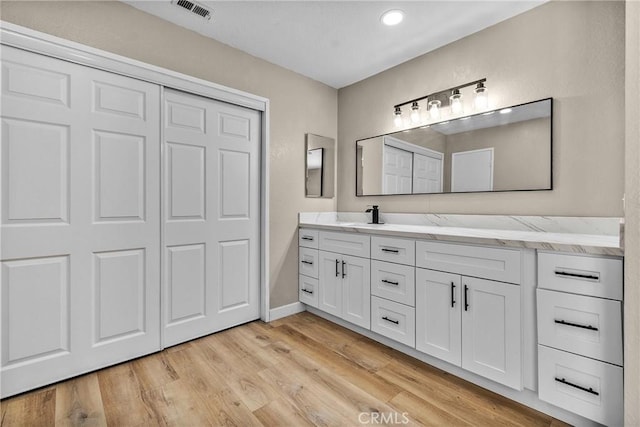 bathroom with visible vents, a sink, recessed lighting, double vanity, and wood finished floors