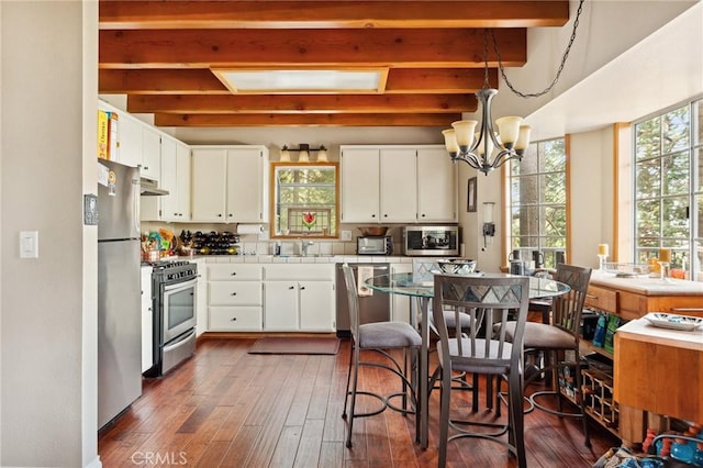 kitchen featuring a notable chandelier, white cabinets, beam ceiling, stainless steel appliances, and a sink