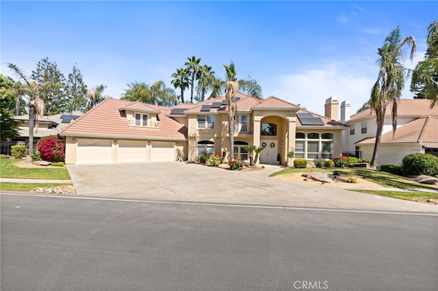 mediterranean / spanish-style house featuring a tiled roof, driveway, roof mounted solar panels, an attached garage, and stucco siding