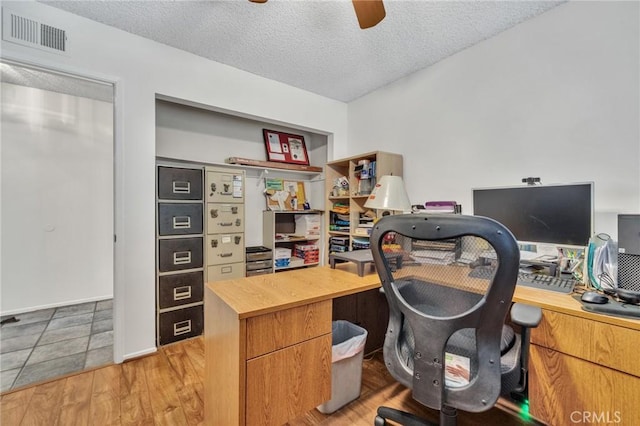 office area featuring light wood-type flooring, visible vents, a textured ceiling, and ceiling fan